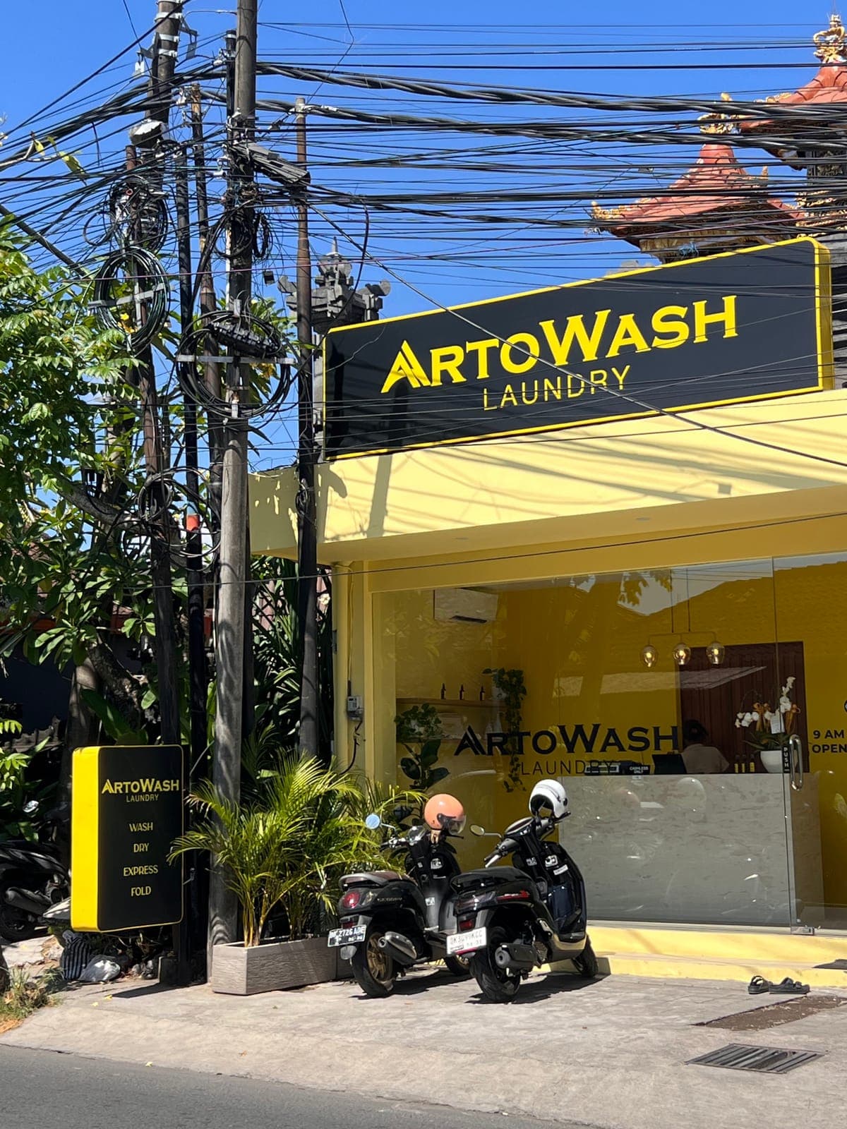 The ArtoWash Laundry shopfront in Bali: yellow walls under a black and yellow sign